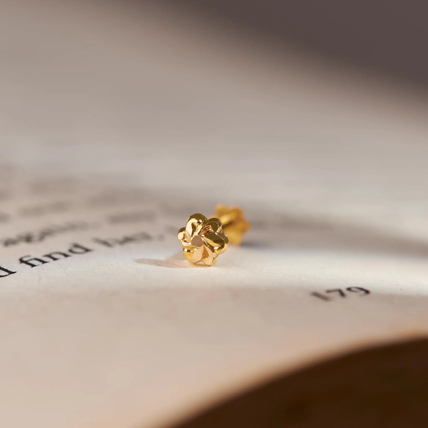 Close up view of a floral 18K gold nose pin placed on an open book page highlighting its intricate design and polished finish