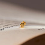 Close up of a delicate gold nose pin placed on an open book highlighting its tiny size and refined detailing