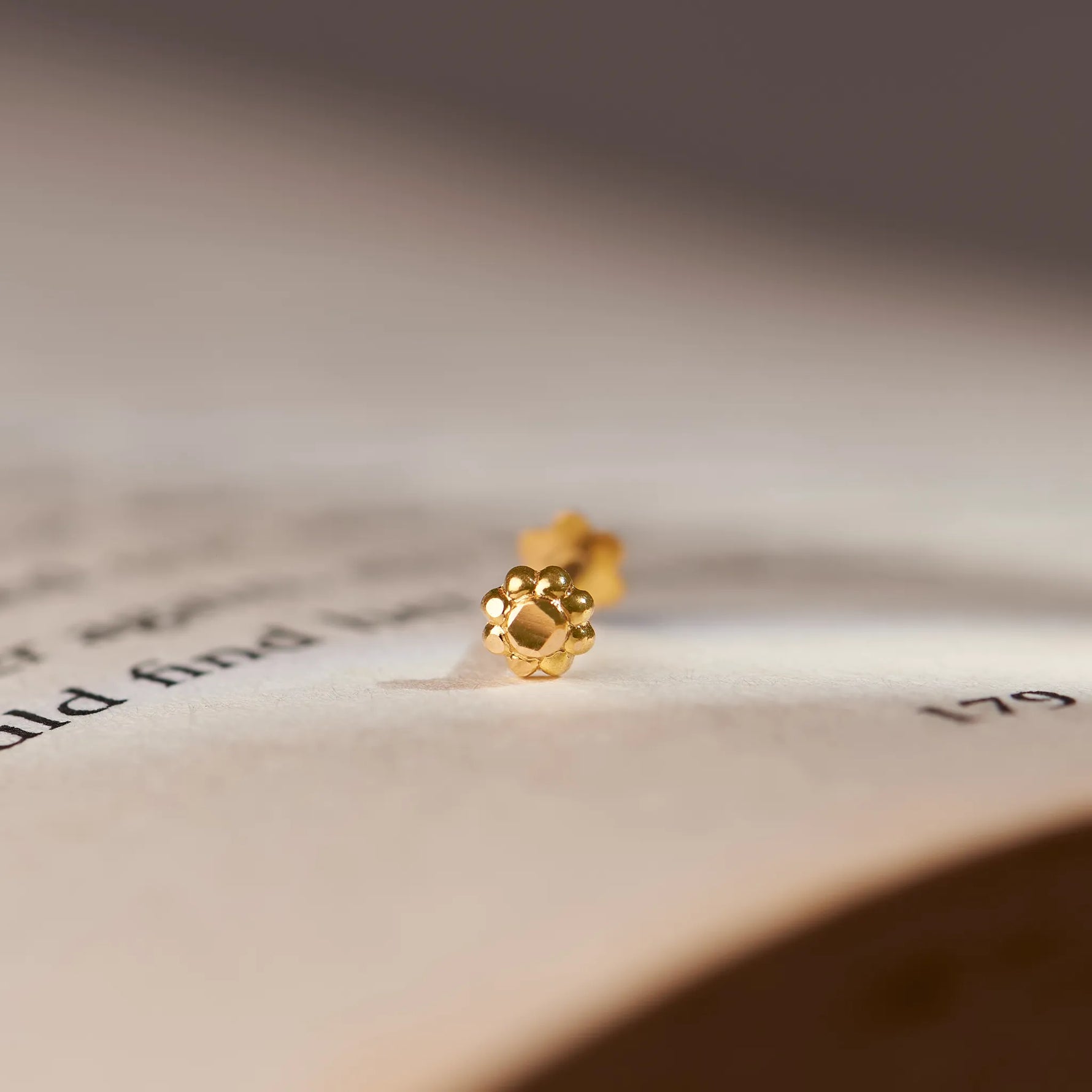 Close up of a delicate gold nose pin placed on an open book highlighting its tiny size and refined detailing