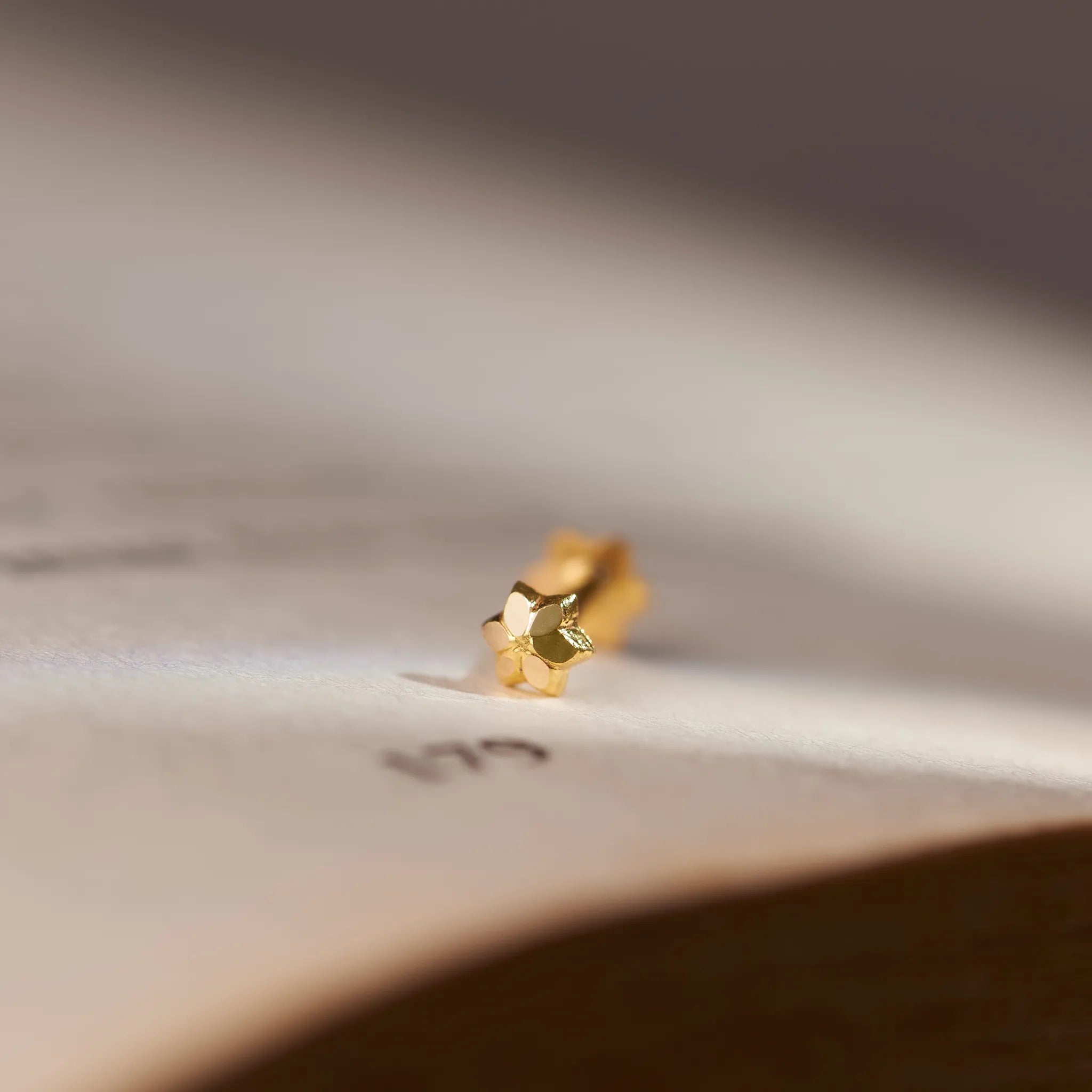 Close up view of a minimal 18K gold nose pin placed on an open book page highlighting its smooth finish and delicate design