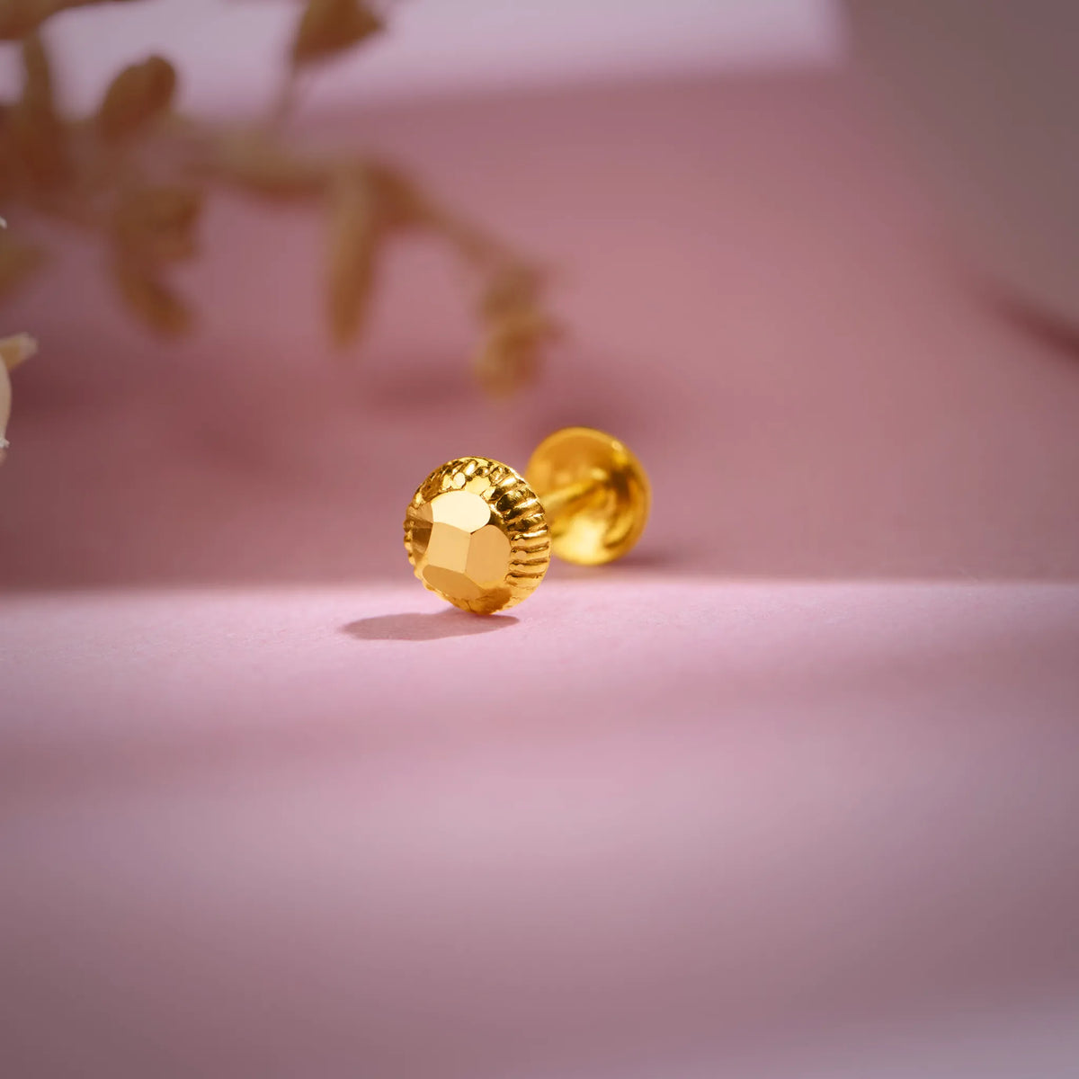 Gold textured 18K nose pin gold placed on a soft pink background highlighting its shine