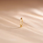 Close up of zigzag patterned 18K gold nose ring standing upright on a soft beige fabric background with warm natural light