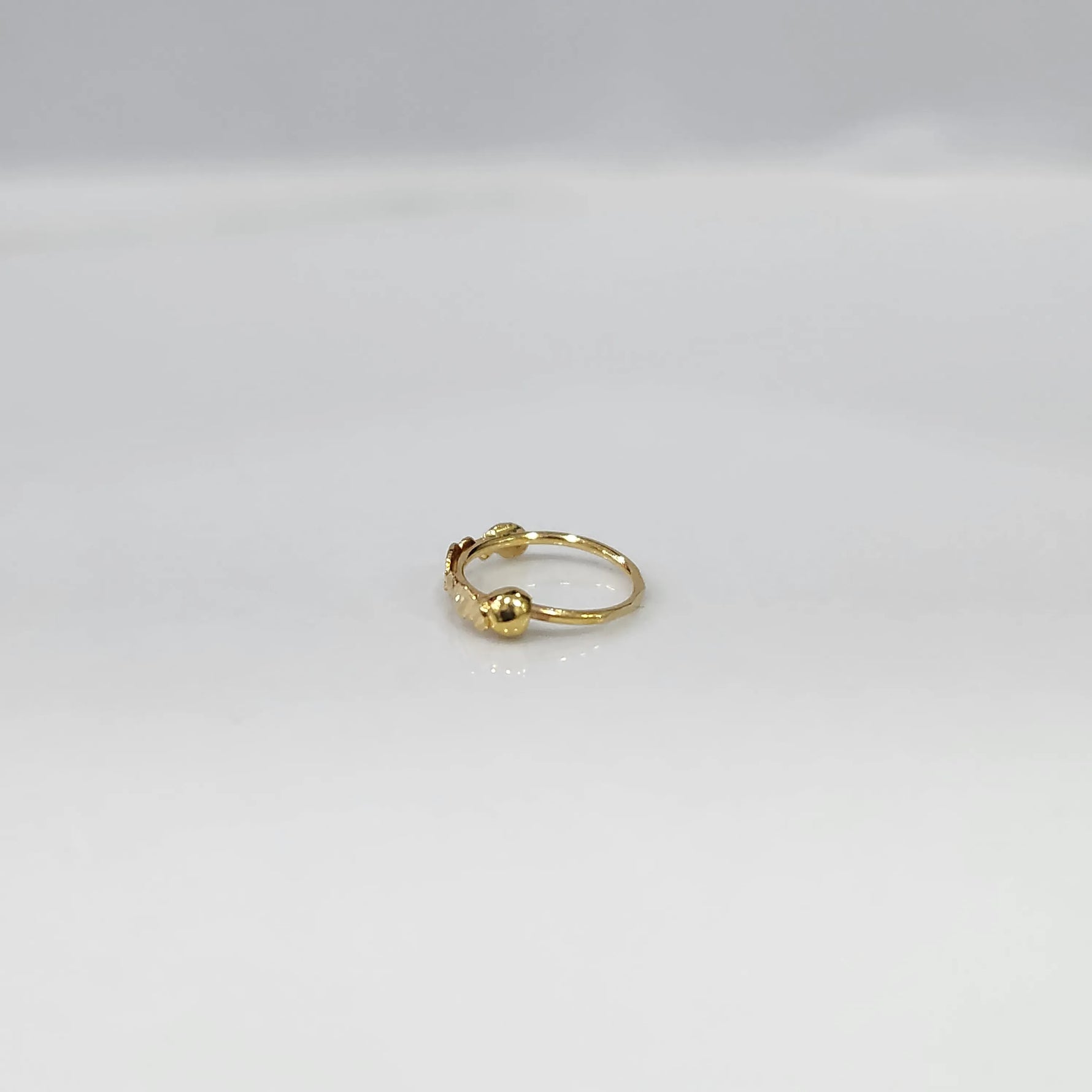 Side angle view of a delicate gold nose ring on a white background emphasizing its slim lightweight design