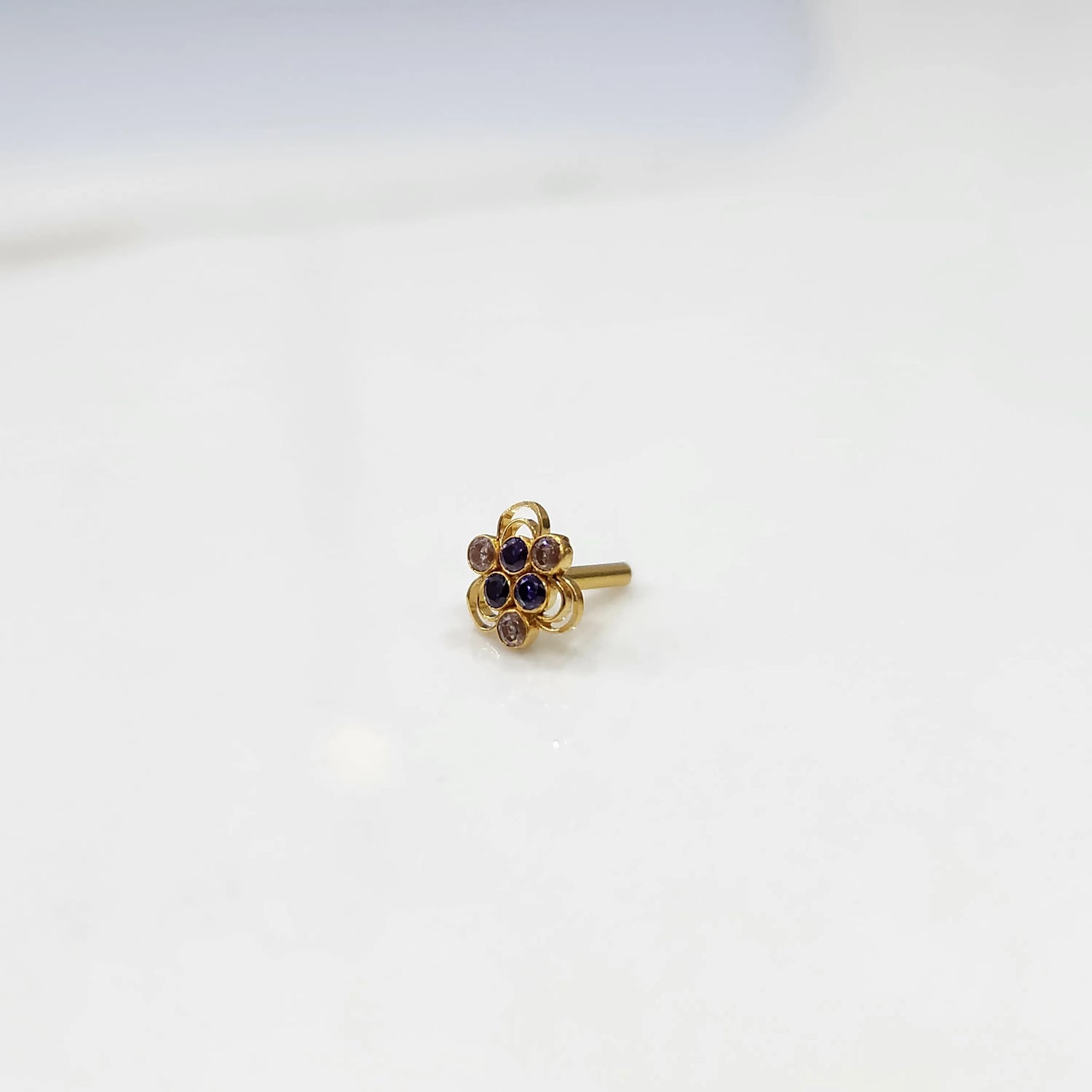 Close up of a floral stone gold nose pin placed on a white surface highlighting the clustered stone design