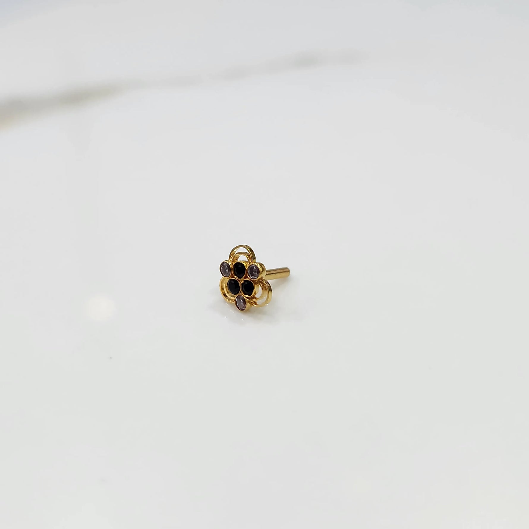Side tilted view of the stone gold nose pin on a white surface focusing on depth and setting height