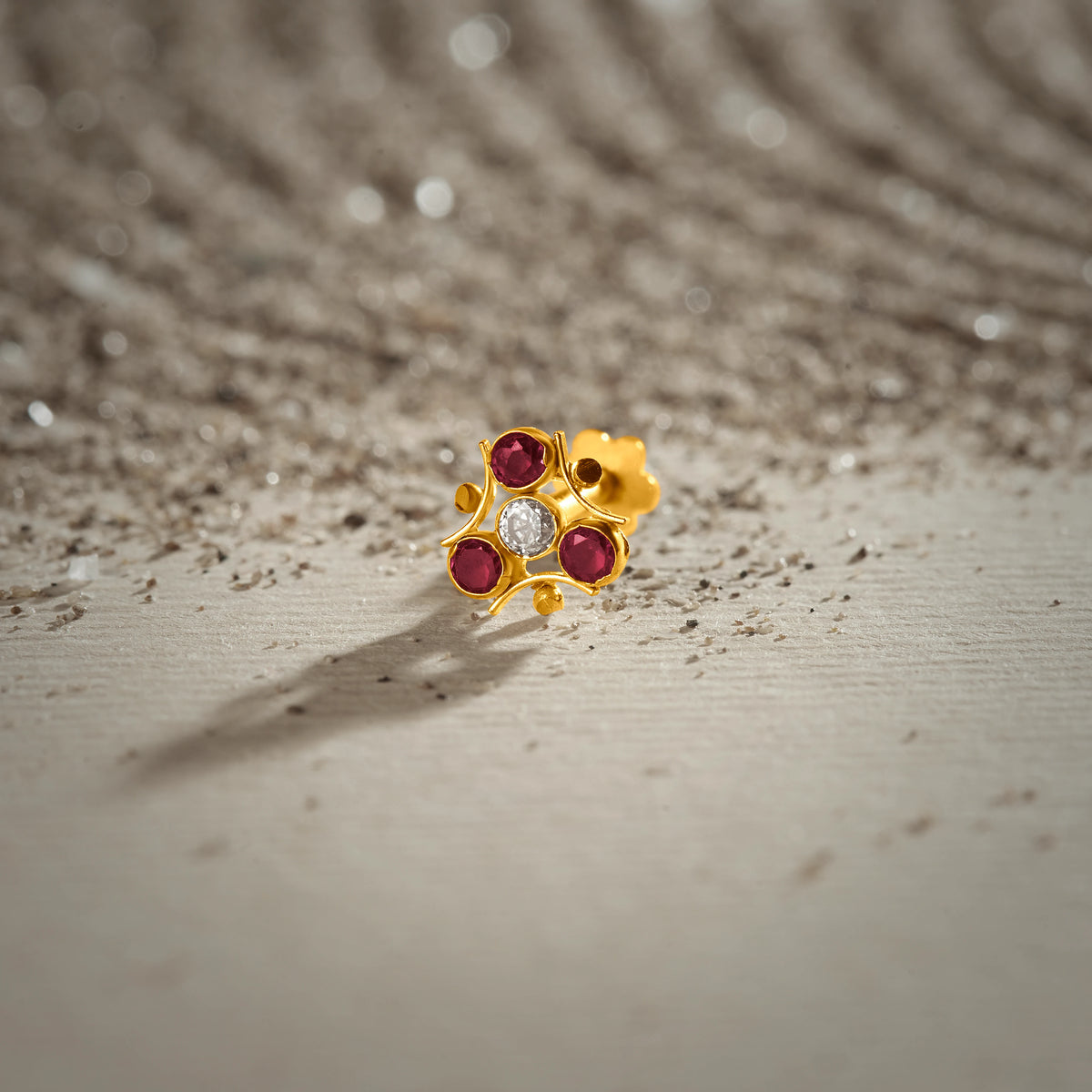 Tiny nose pin gold floral stones on textured surface