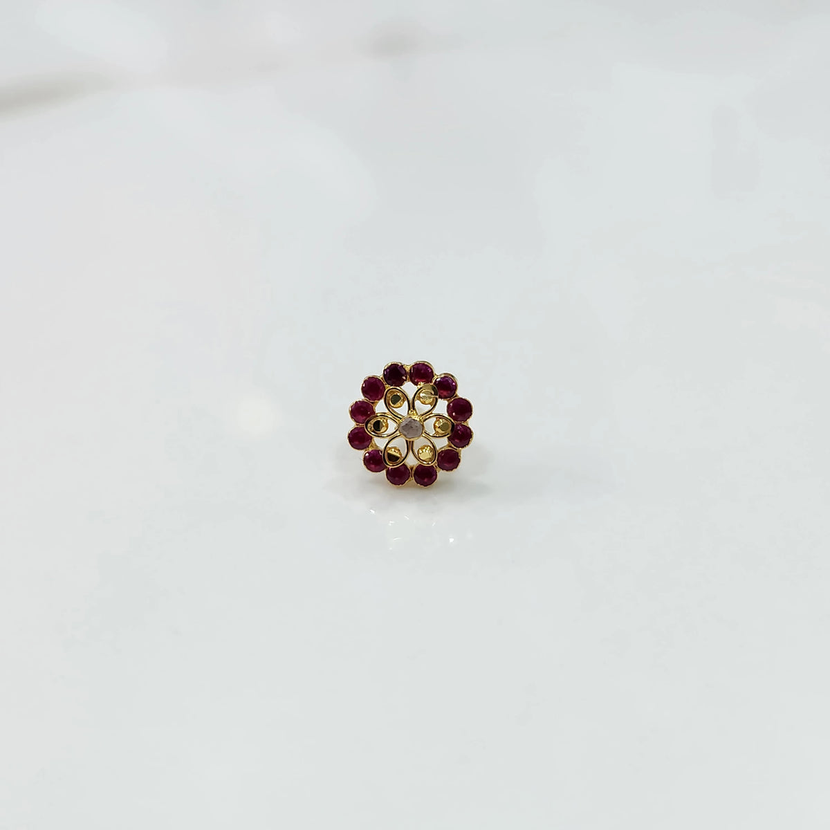 Gold nose pin design with red stone floral pattern on white background