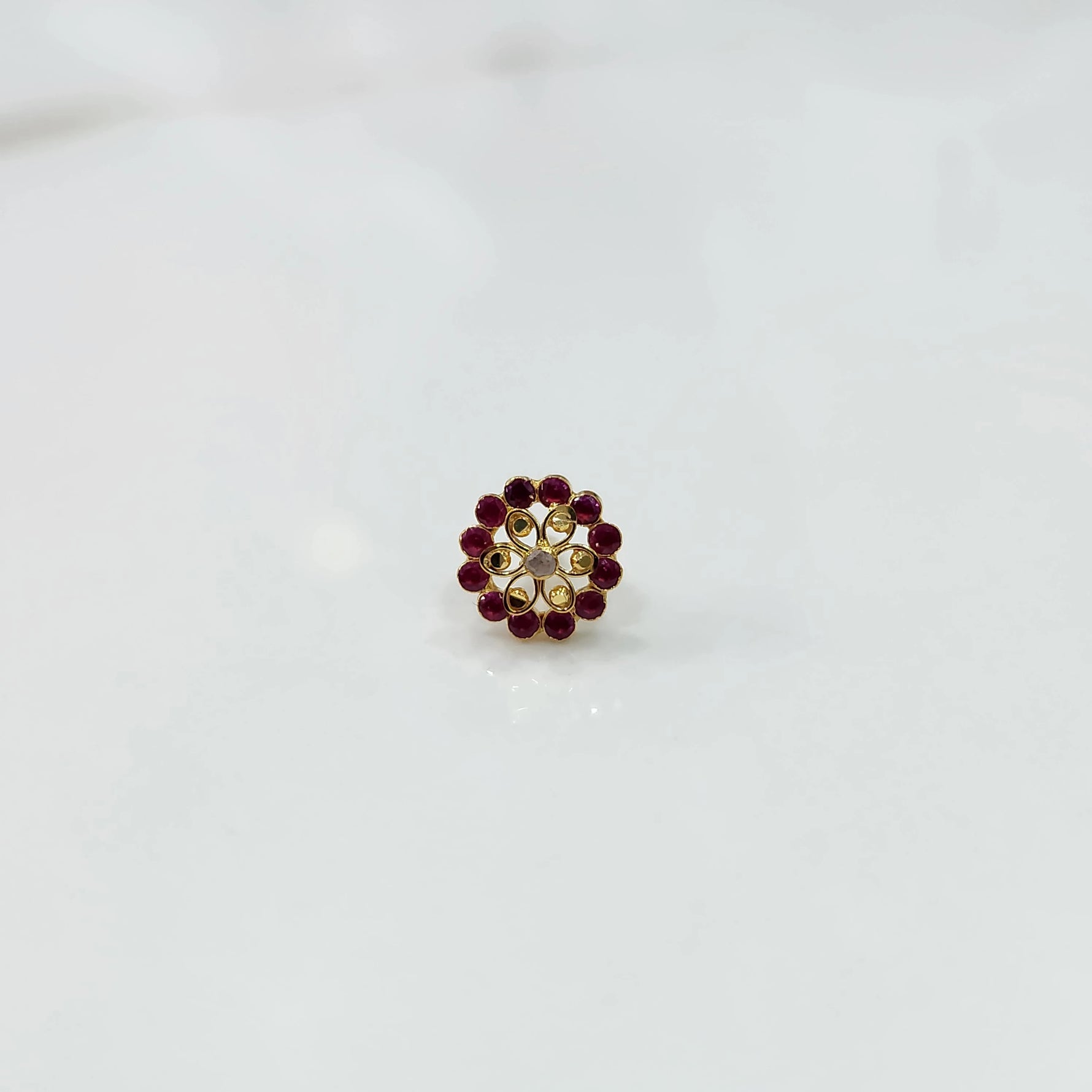Gold nose pin design with red stone floral pattern on white background