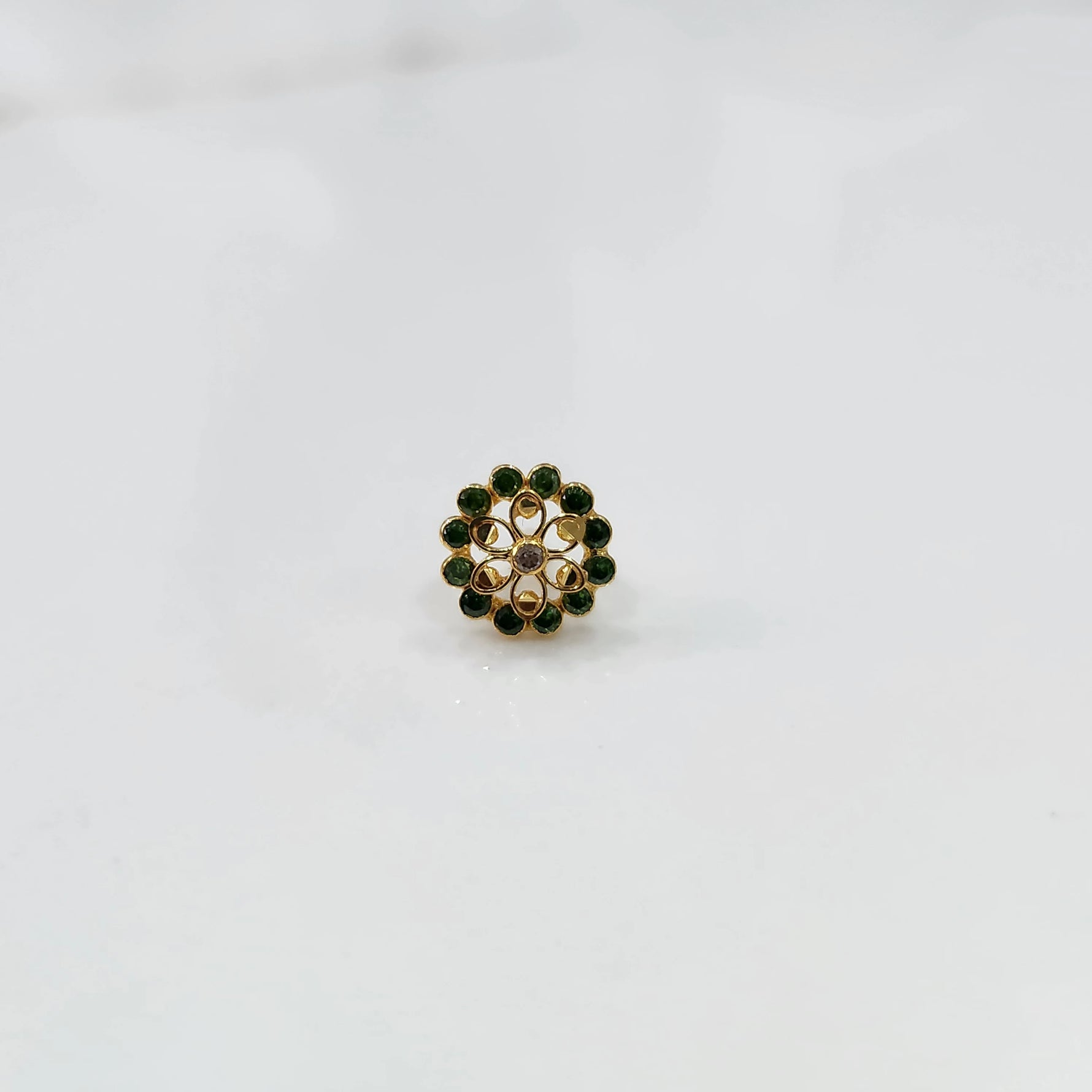 Gold nose pin design with green stone floral cluster on white background