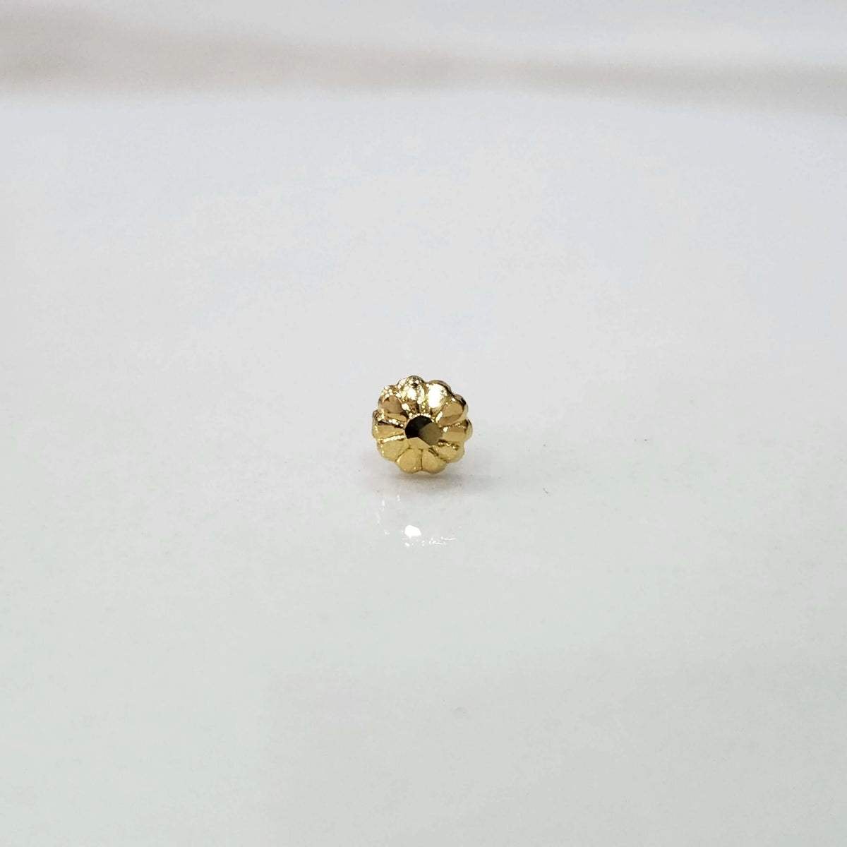 Close view of a tiny gold nose pin placed on a white surface highlighting its fine craftsmanship