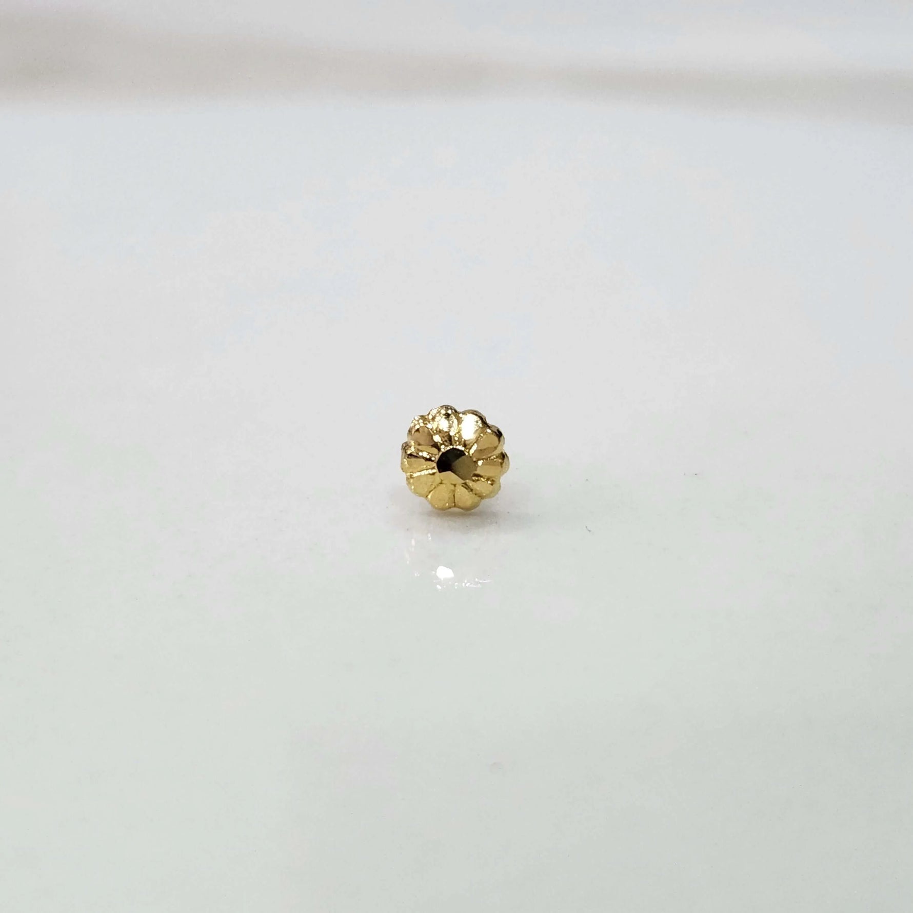 Close view of a tiny gold nose pin placed on a white surface highlighting its fine craftsmanship