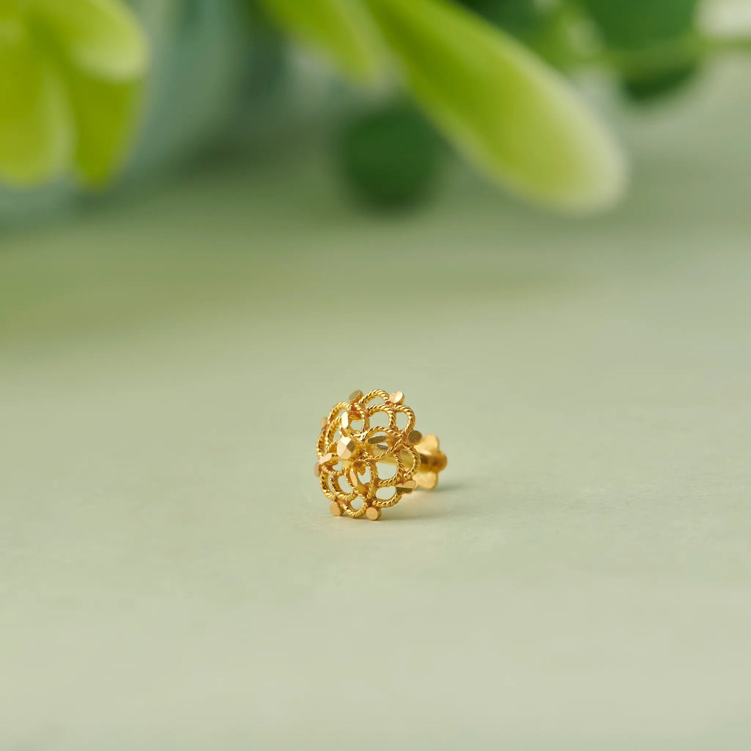 Close up of floral gold nose pin resting on a soft green background with blurred leaves