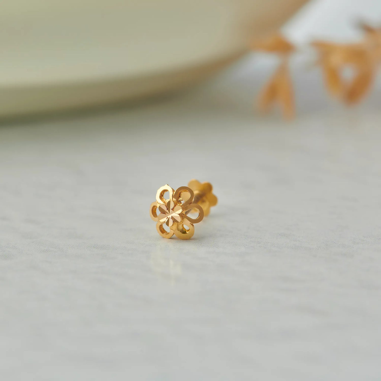Close up of floral gold nose pin placed on a soft white surface highlighting delicate craftsmanship