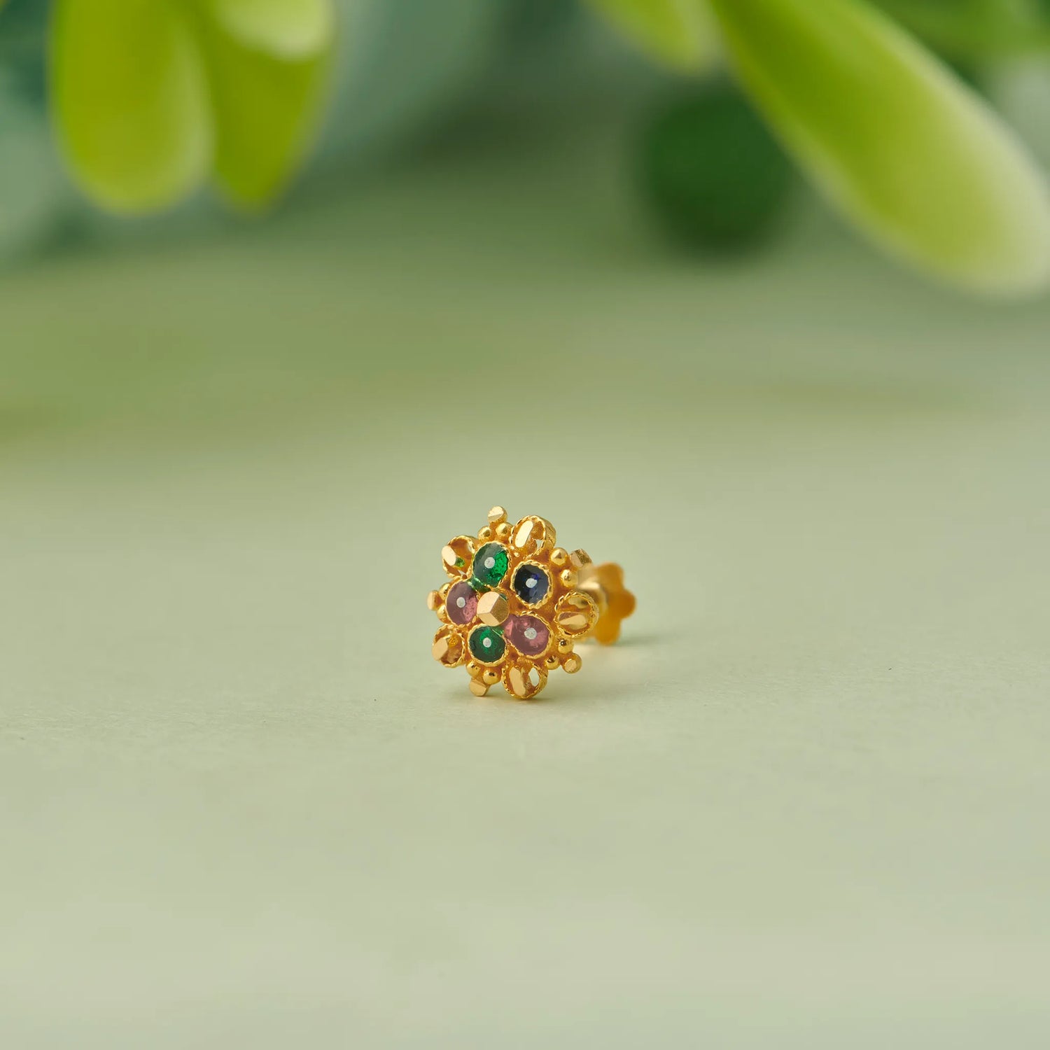 Close up of floral gold nose pin with green stone accents placed on a soft green background