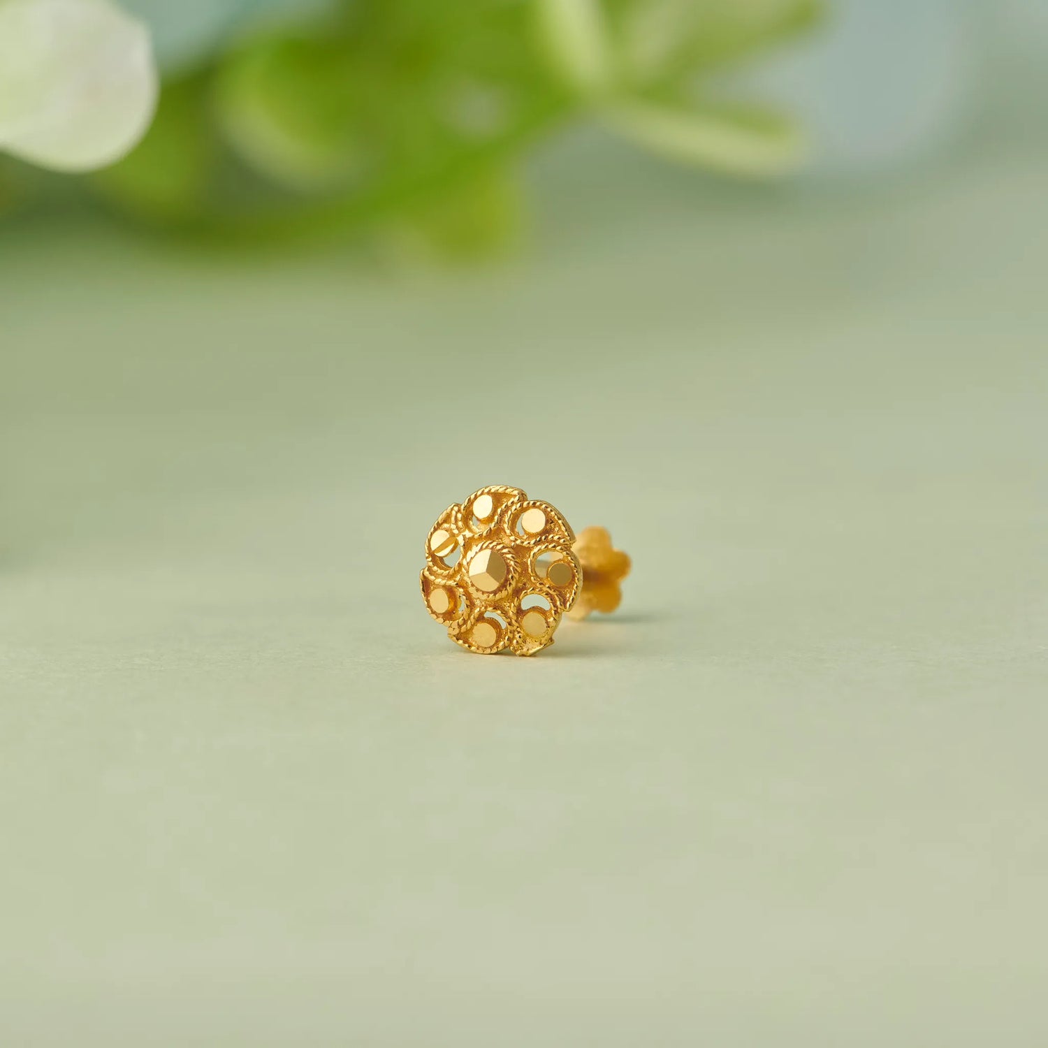 Close up view of an intricate floral pattern 18K gold nose pin placed on a soft green background showcasing fine craftsmanship