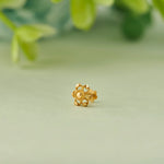 Close up of floral 18K gold nose pin placed on a soft green background highlighting intricate cutwork design