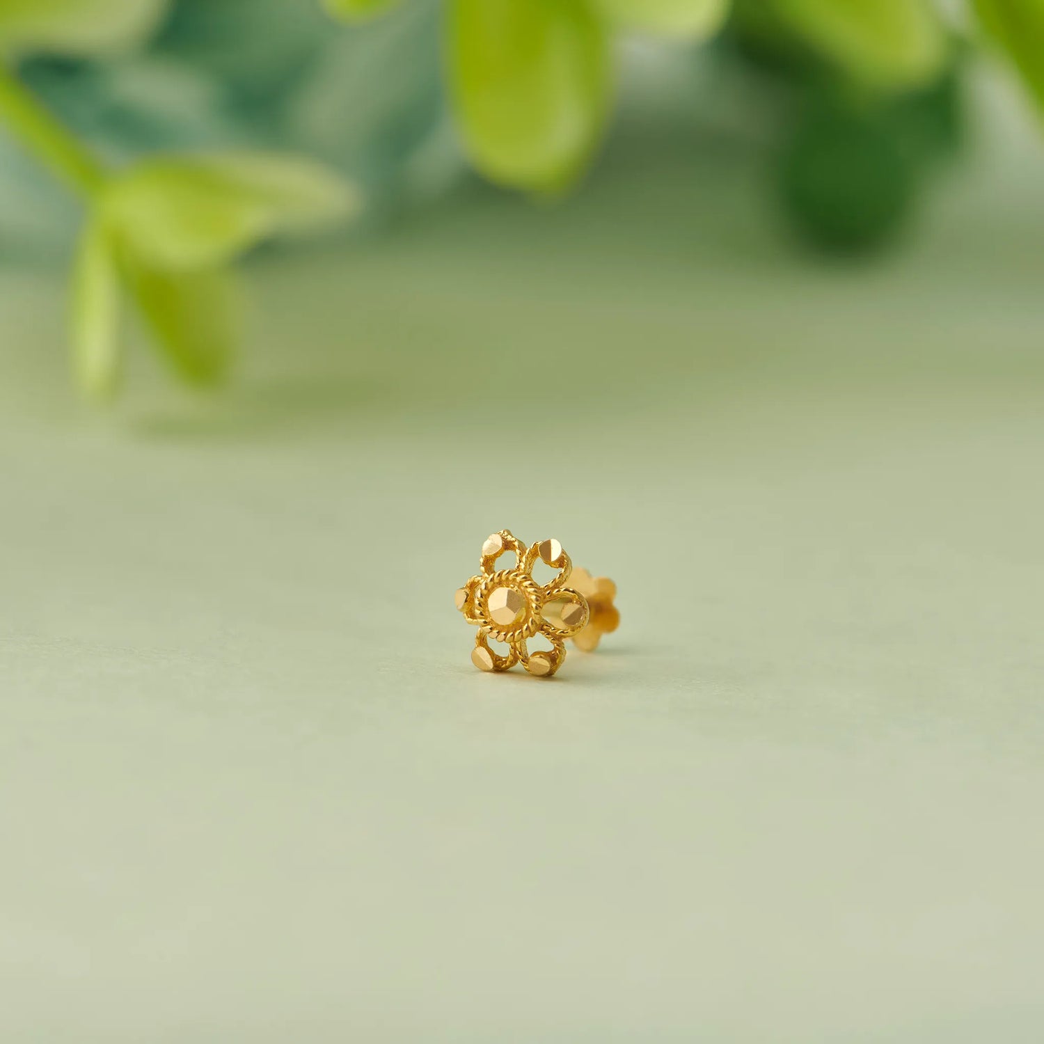 Close up of floral 18K gold nose pin placed on a soft green background highlighting intricate cutwork design