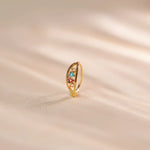 Close up of multicolour stone 18K gold nose ring standing upright on a soft beige fabric surface with gentle light reflections