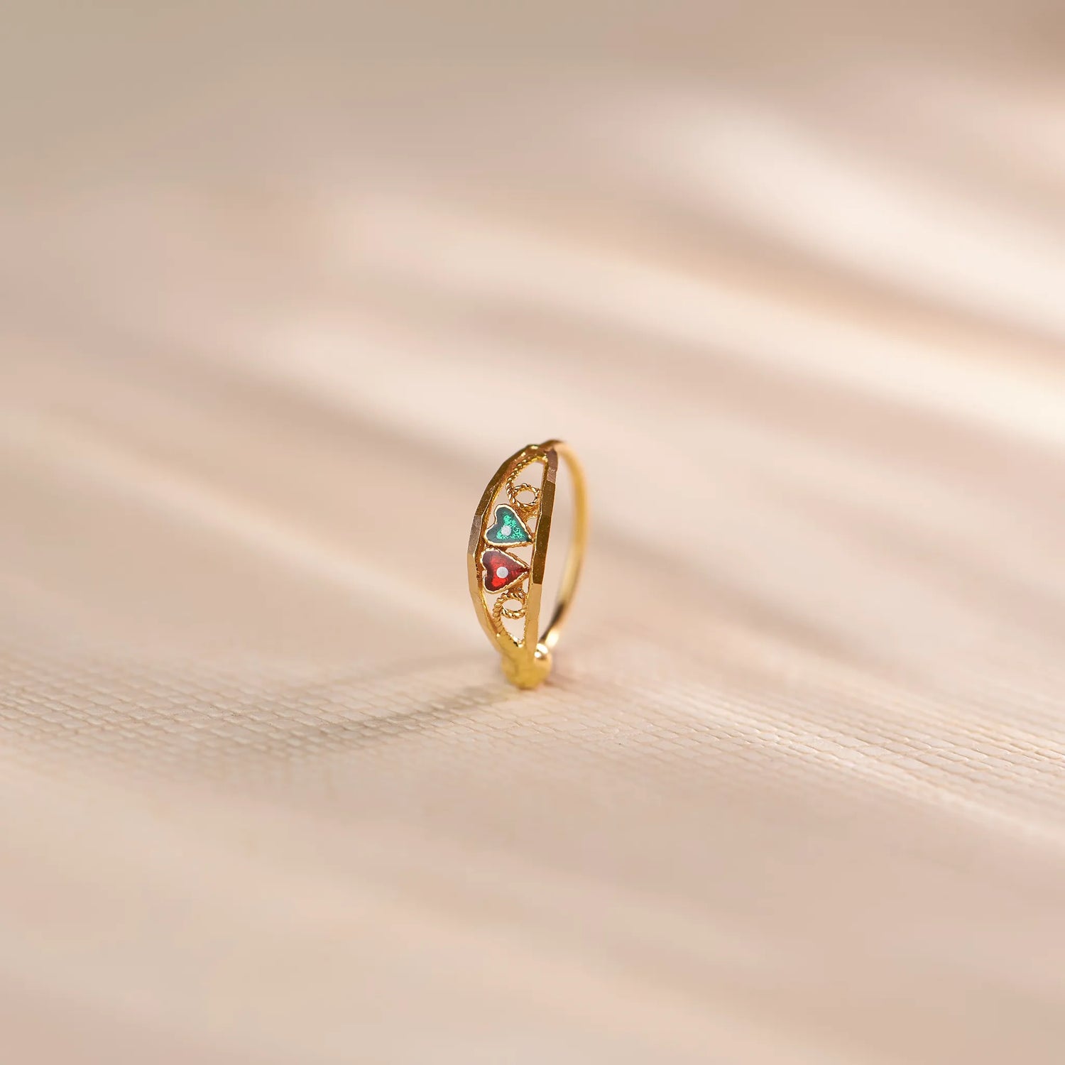 Close up of multicolour stone 18K gold nose ring standing upright on a soft beige fabric surface with gentle light reflections