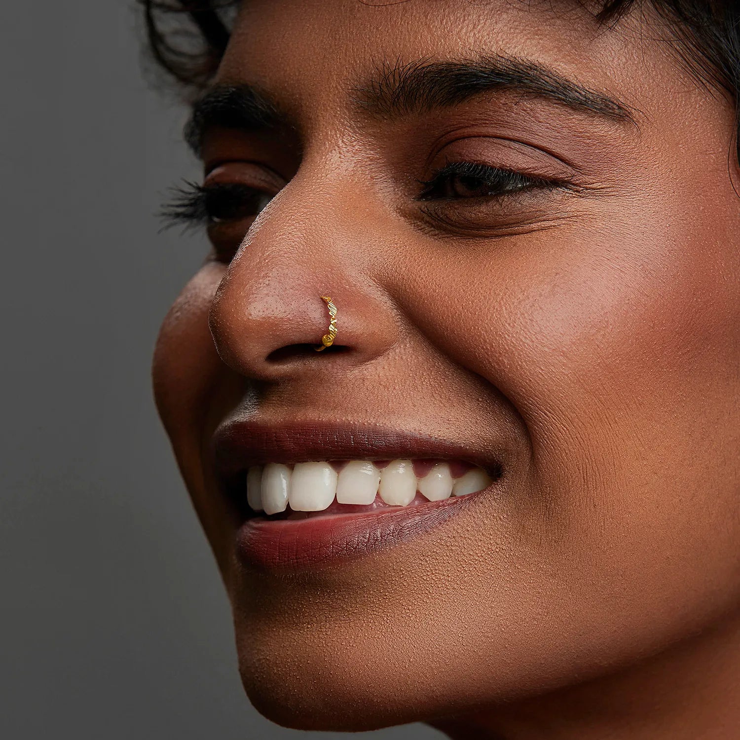 Smiling woman wearing a small gold nose ring highlighting a modern and confident look