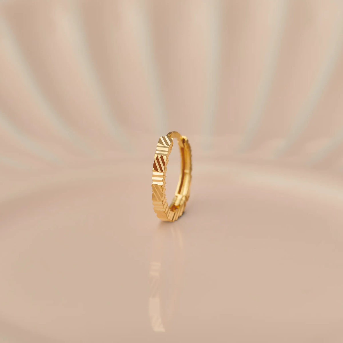 Close up of textured 18K gold nose ring standing upright on a soft beige background with subtle light reflections