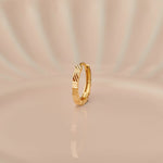 Close up of textured 18K gold nose ring standing upright on a soft beige background with subtle light reflections