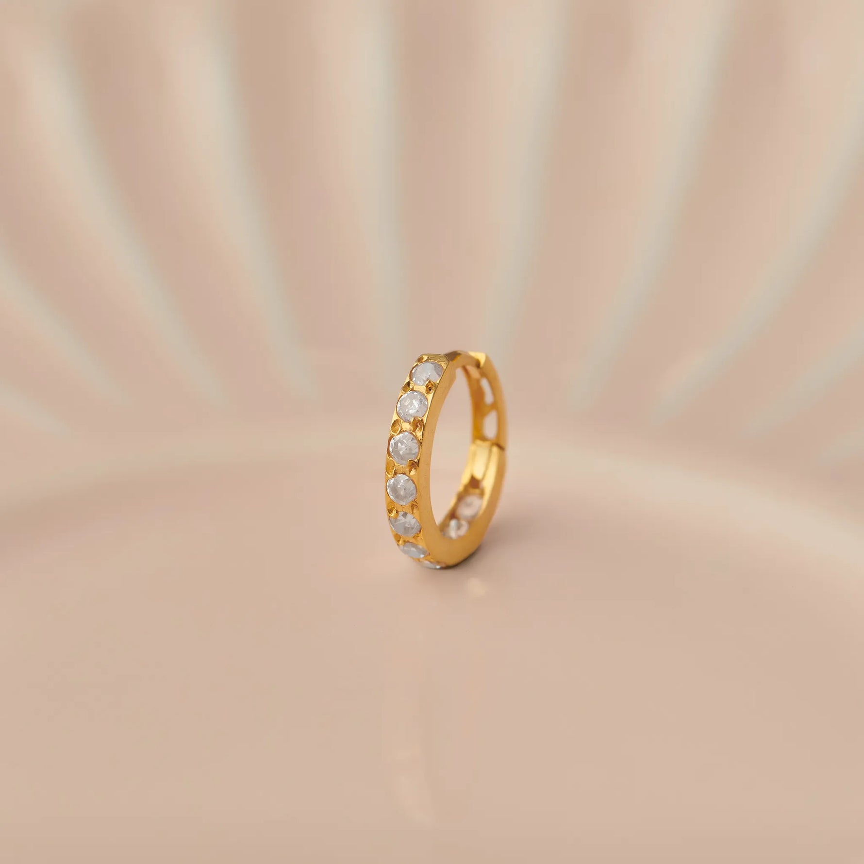 Gold nose ring standing upright on a peach toned surface emphasizing slim band profile