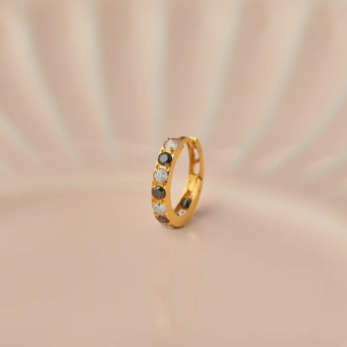 Close up of 18K gold hoop nose ring with black and clear stones placed on a soft beige background highlighting gemstone detailing