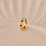 Close up of 18K gold hoop nose ring with black and clear stones placed on a soft beige background highlighting gemstone detailing