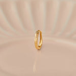 Side view of textured 18K gold hoop nose ring standing upright on a soft beige background with gentle light rays