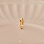 Side view of minimalist 18K gold hoop nose ring standing upright on a soft beige background with subtle light reflections