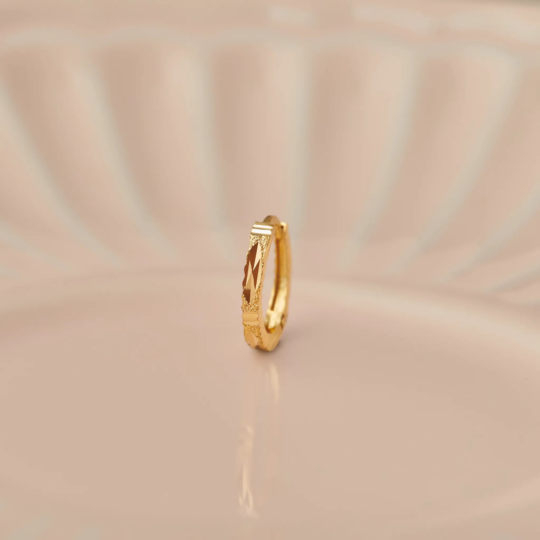Side view of minimalist 18K gold hoop nose ring standing upright on a soft beige background with subtle light reflections