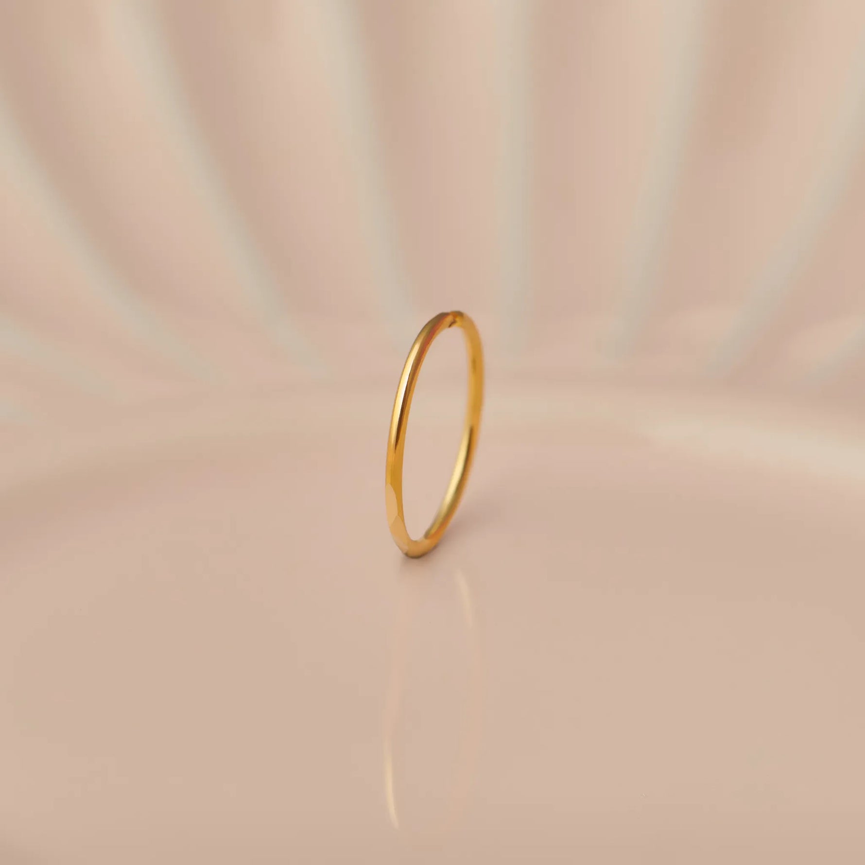 Front view of slim plain 18K gold hoop nose ring standing upright on a soft beige background with subtle light reflections