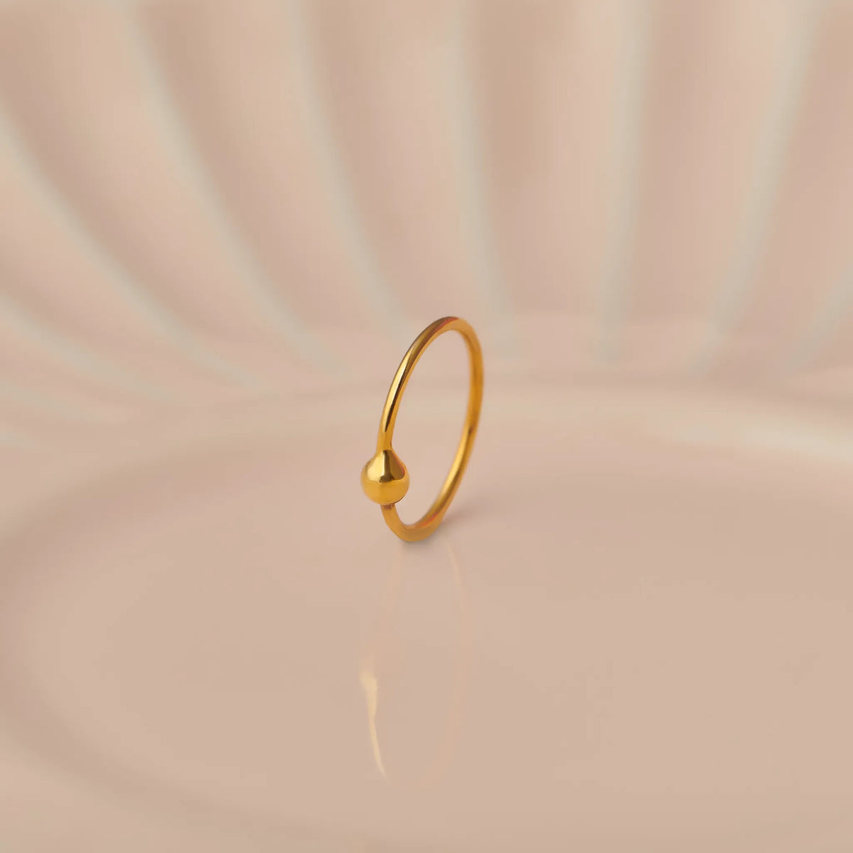 Close up of minimalist open hoop 18K gold nose ring placed on a soft beige background with gentle light reflections