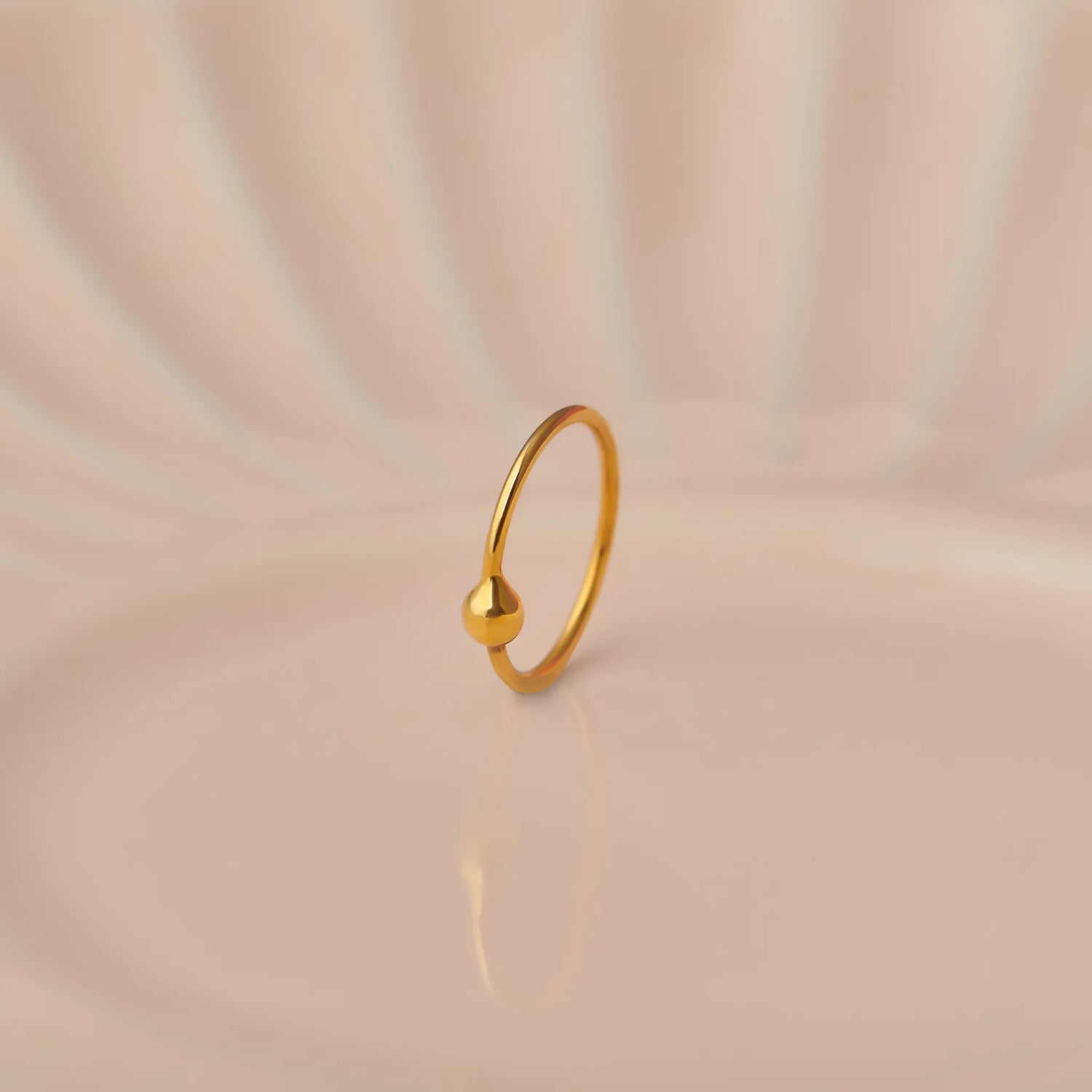 Close up of minimalist open hoop 18K gold nose ring placed on a soft beige background with gentle light reflections