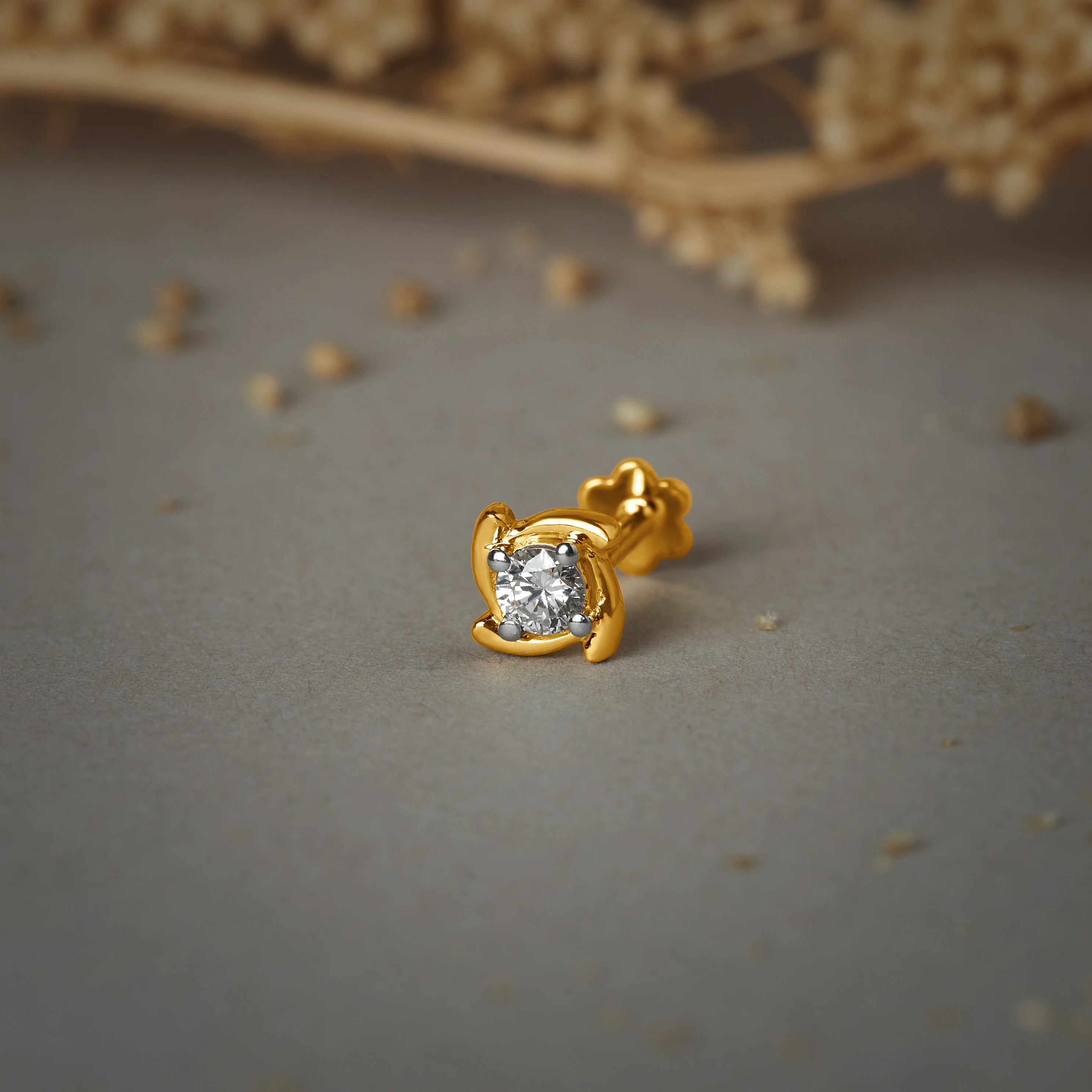 Nose pin gold with heart-shaped design featuring a central sparkling stone set in a polished gold base on a soft neutral background