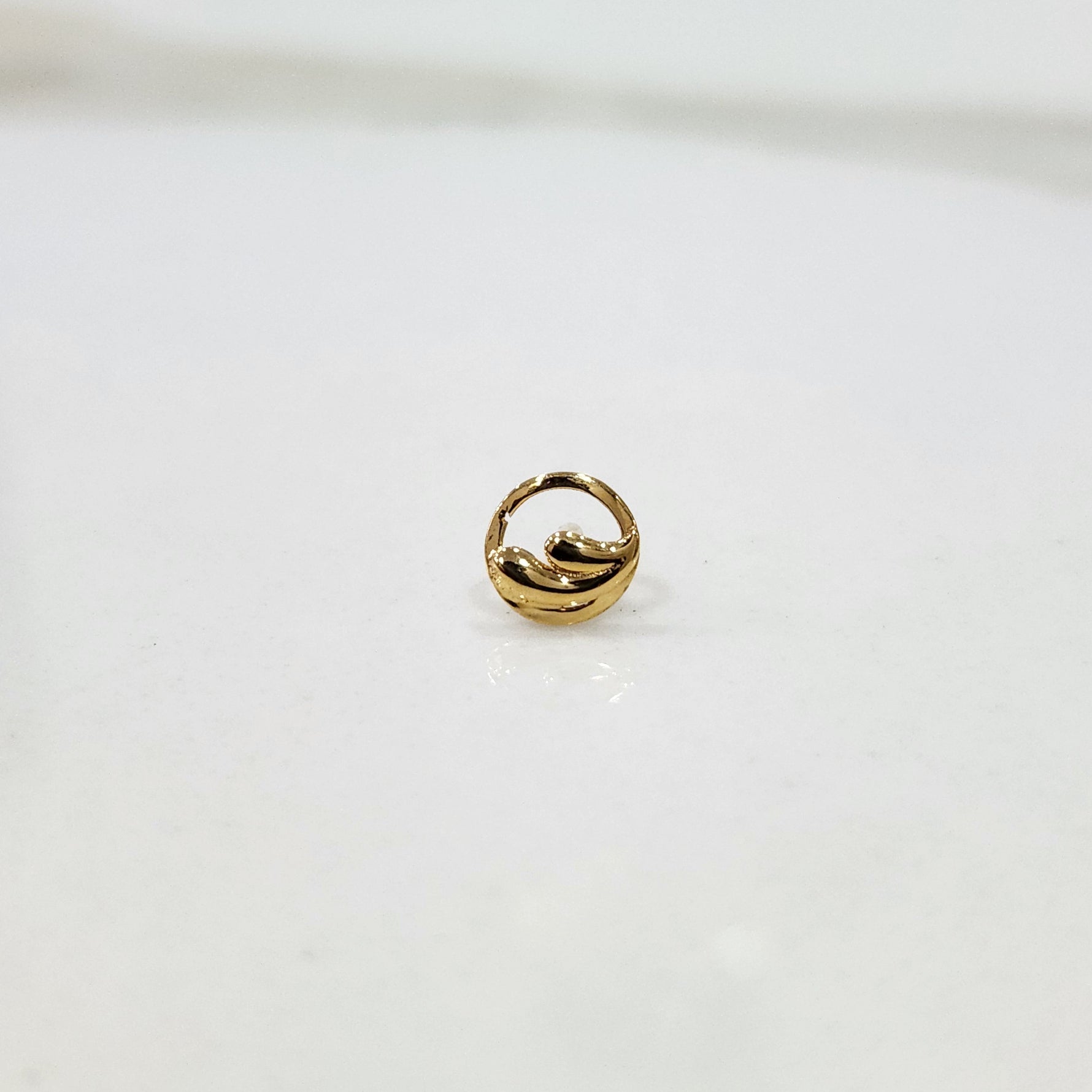 Encircled Waves gold nose pin in 18K gold displayed on plain surface showcasing elegant circular wave design