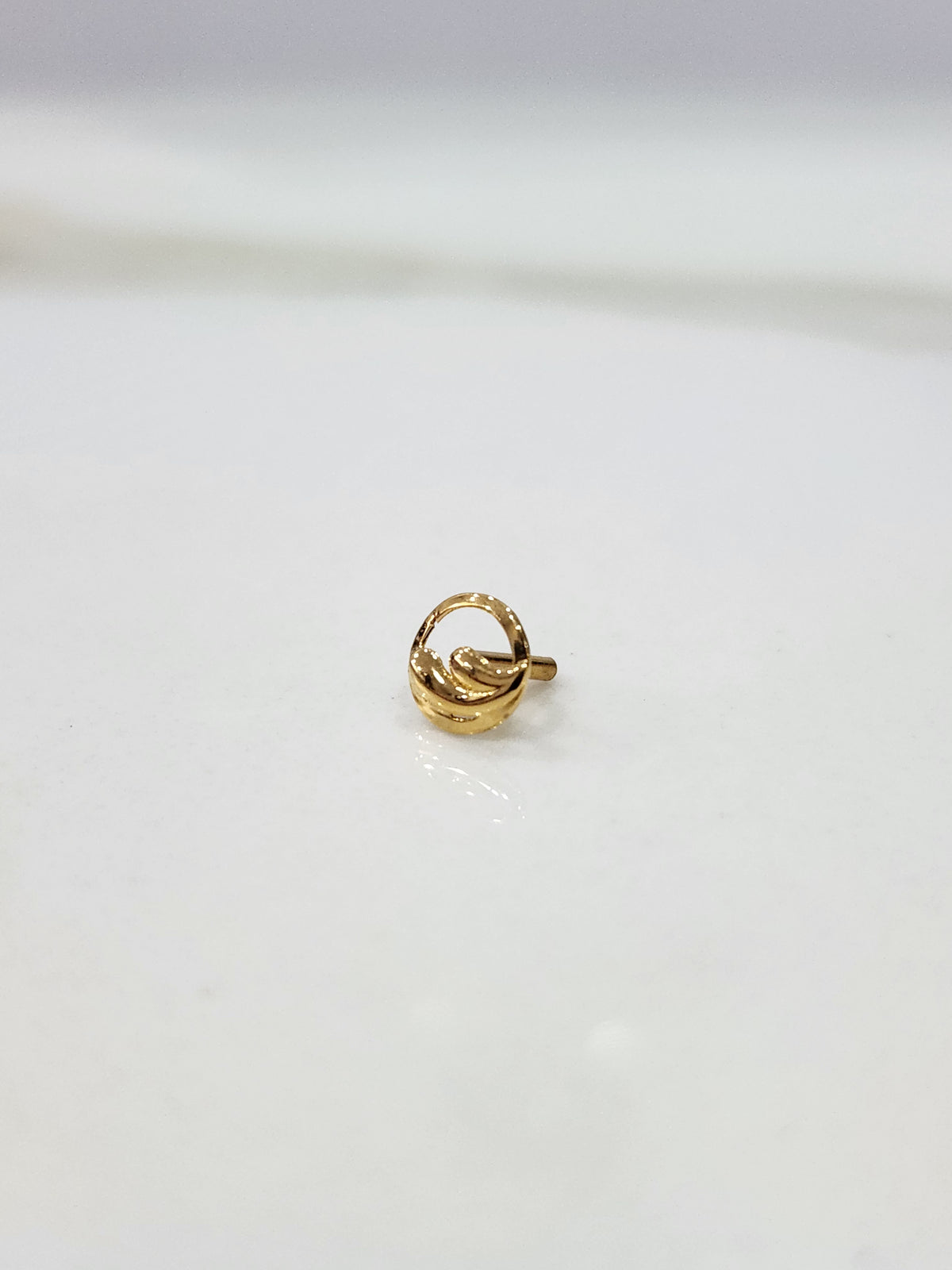 Encircled Waves gold nose pin in 18K gold displayed on a flat surface with elegant wave-inspired circular design