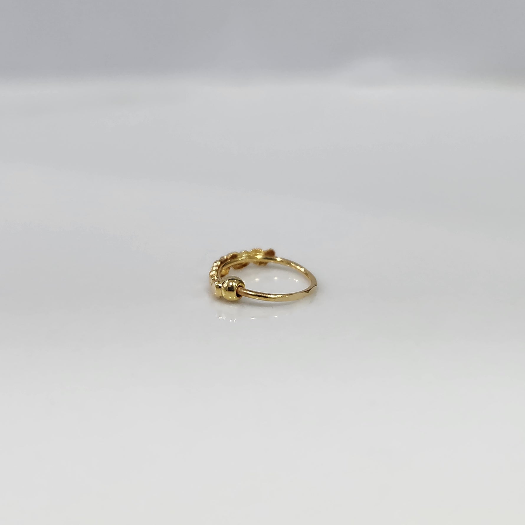 Gold Heart Row gold nose ring in 18K gold with delicate heart pattern, side view on plain background