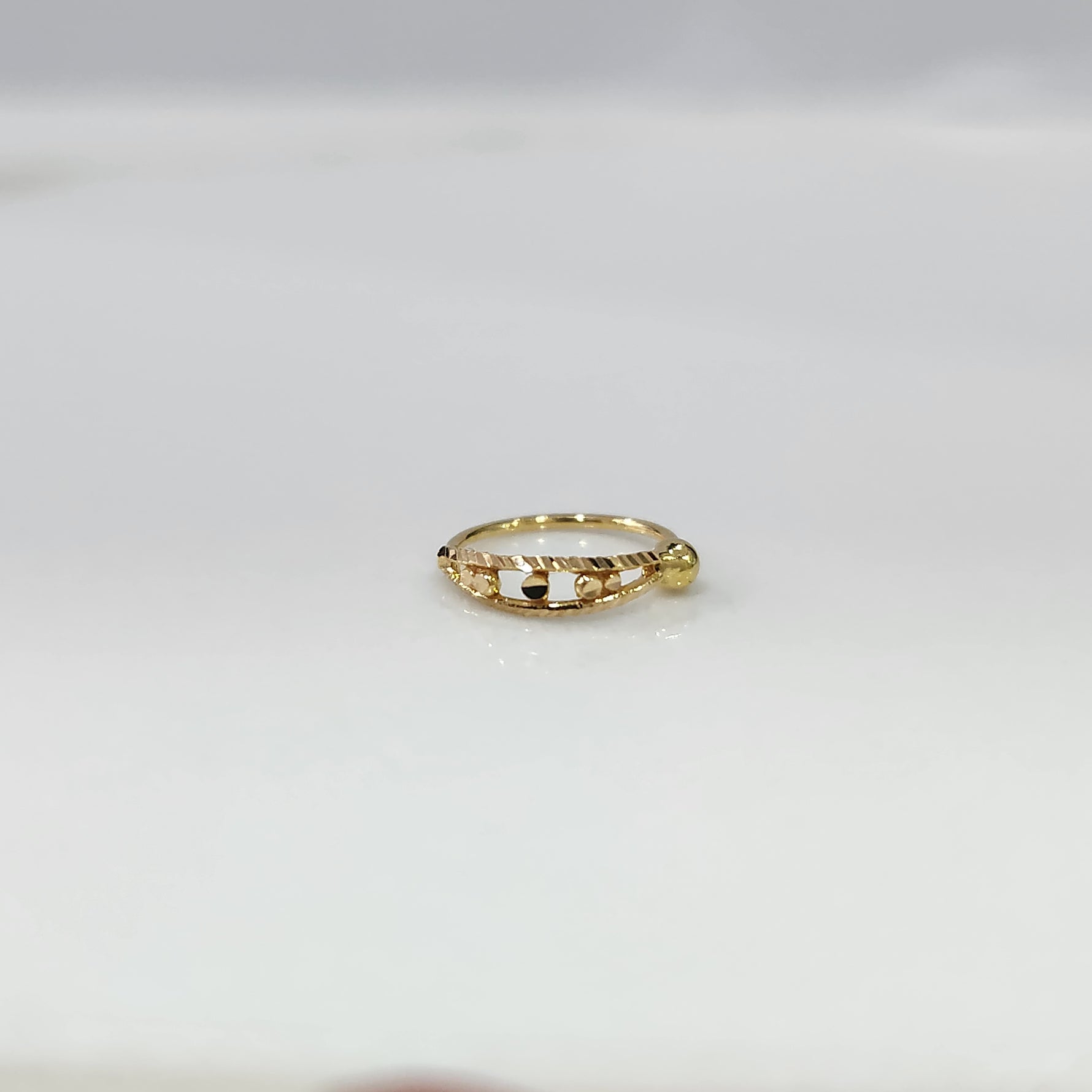 Gold Orbit Gold Nose Ring in 18K gold displayed on a flat surface with intricate orbit-inspired design