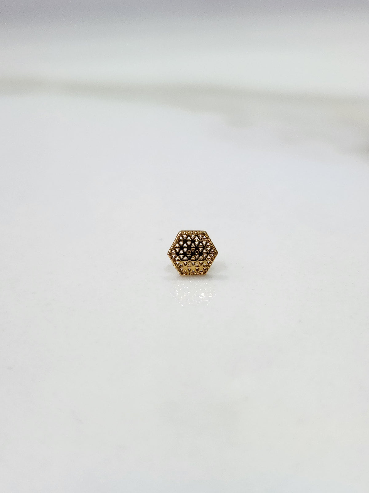 Hexa Lattice gold nose pin in 18K gold with intricate geometric hexagon lattice pattern placed on a flat surface