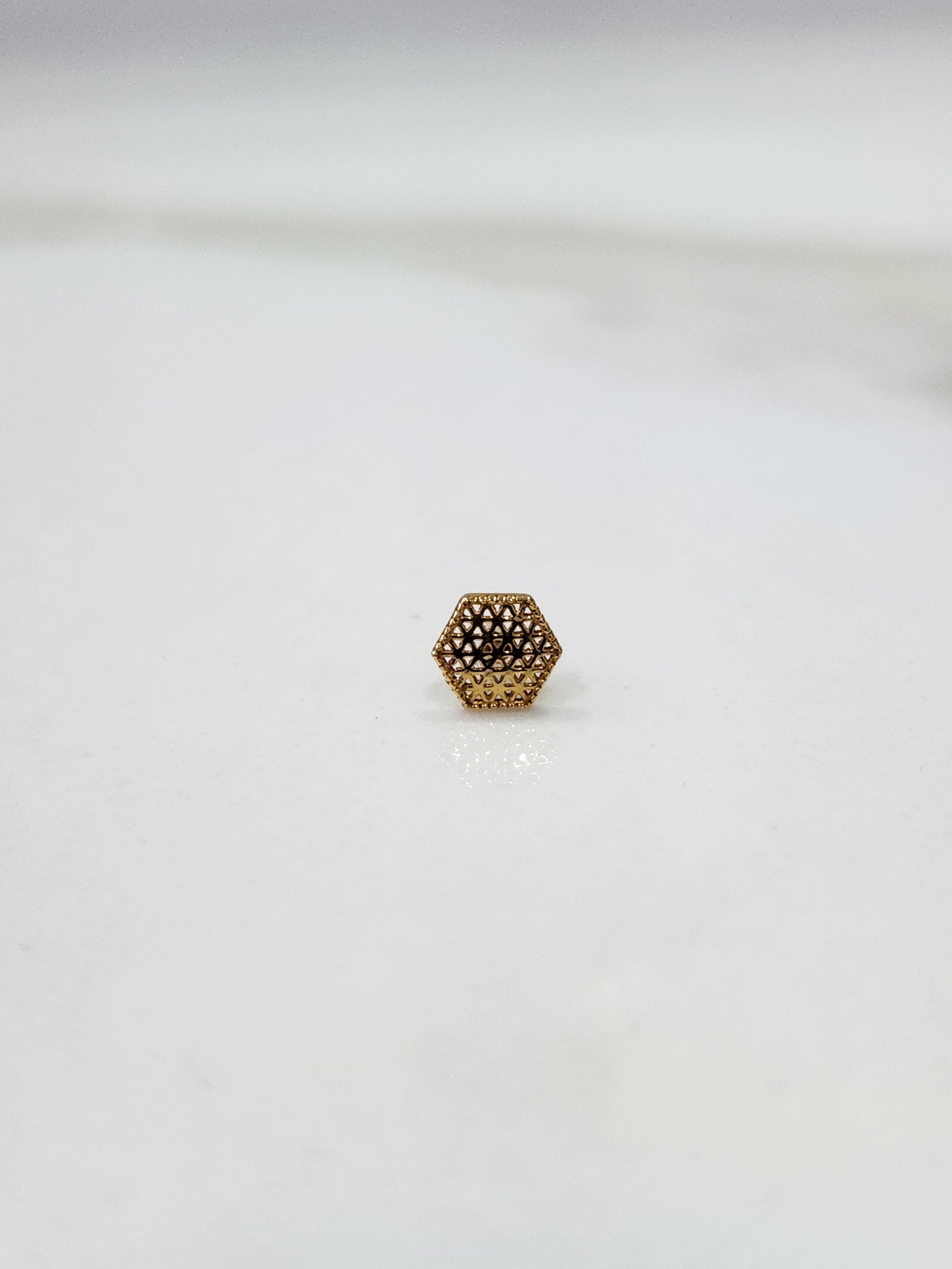 Hexa Lattice gold nose pin in 18K gold with intricate geometric hexagon lattice pattern placed on a flat surface