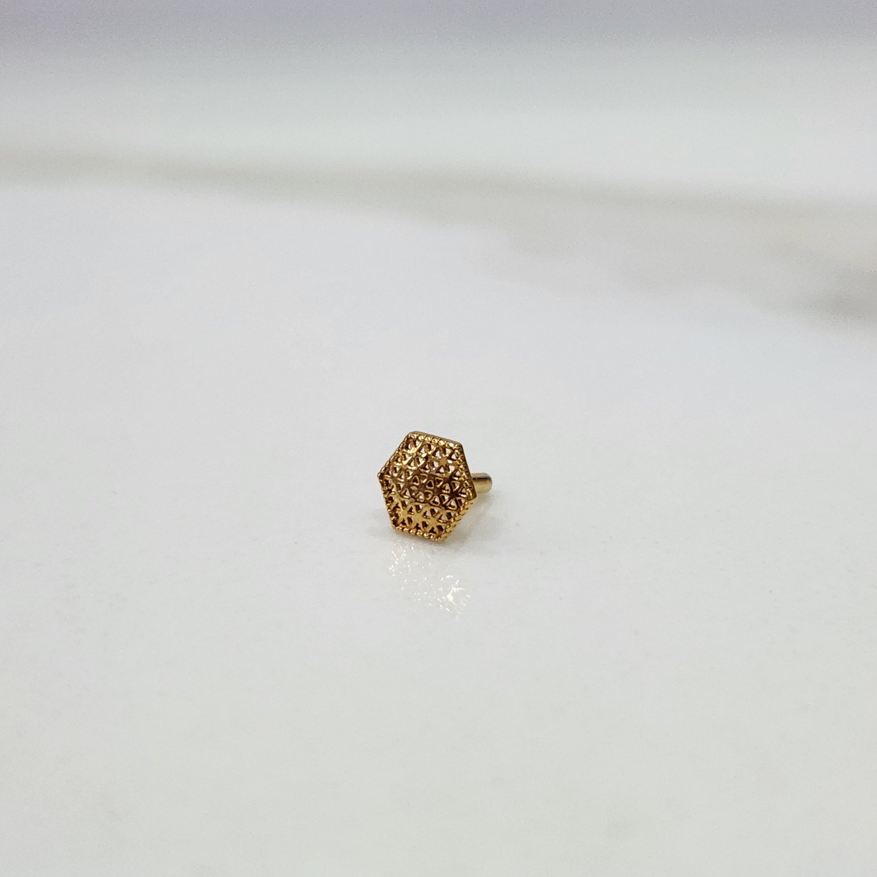 Hexa Lattice gold nose pin crafted in 18K gold with detailed geometric hexagon lattice pattern, side view on flat surface