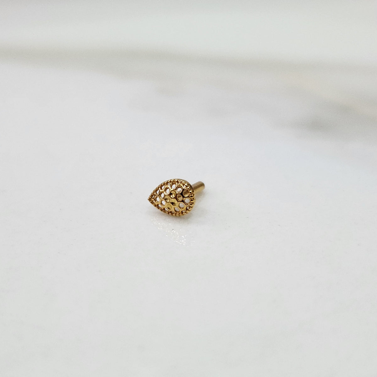Close-up view of Honeycomb Drop gold nose pin in teardrop shape with hexagonal cutout pattern placed on white background