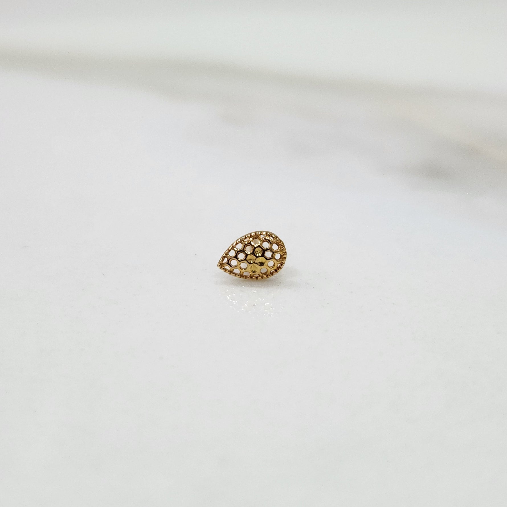Honeycomb Drop gold nose pin in teardrop design with intricate hexagonal cutouts placed on a white surface