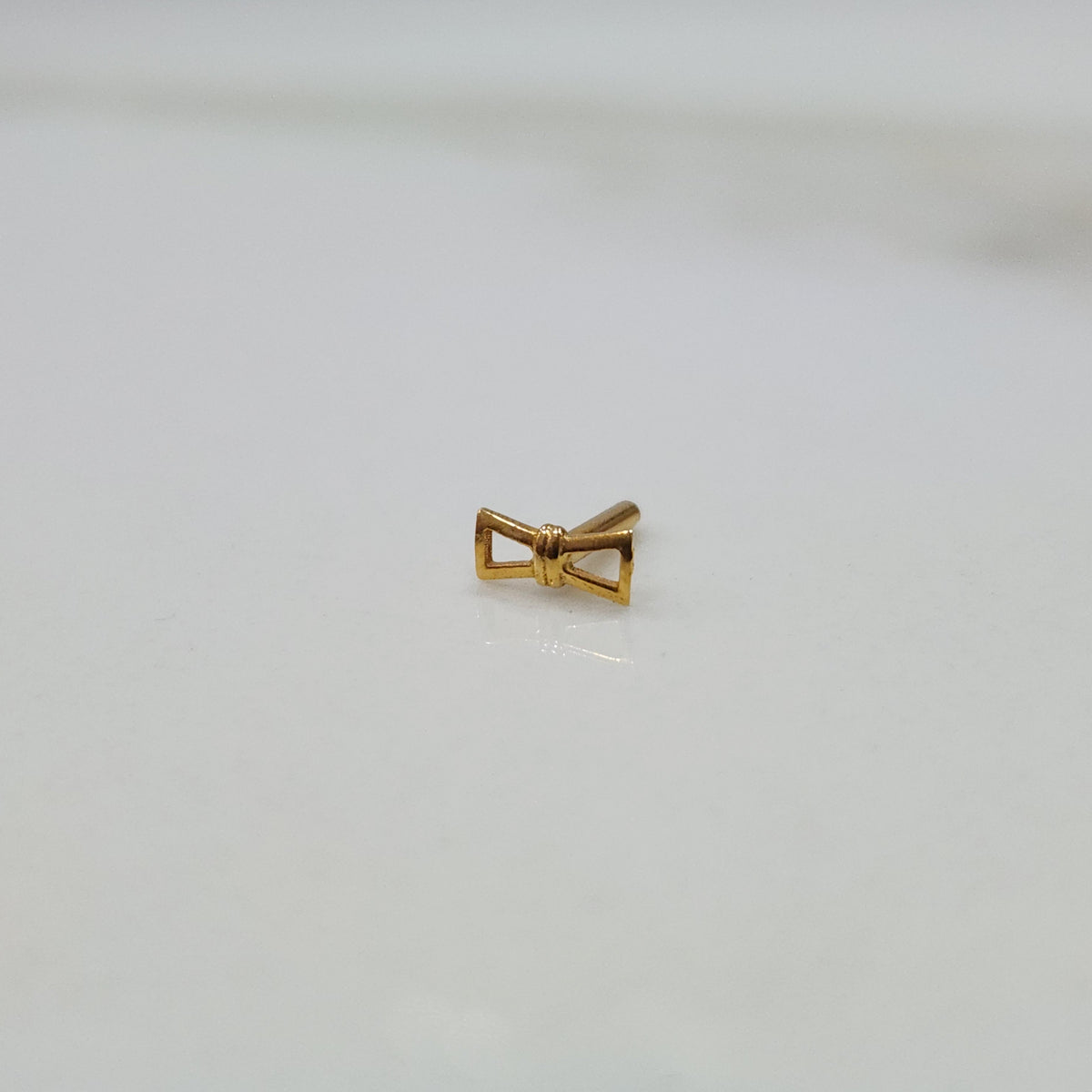 Ribbon Whisper gold nose pin with delicate bow-tie inspired design placed on a flat surface in close-up view