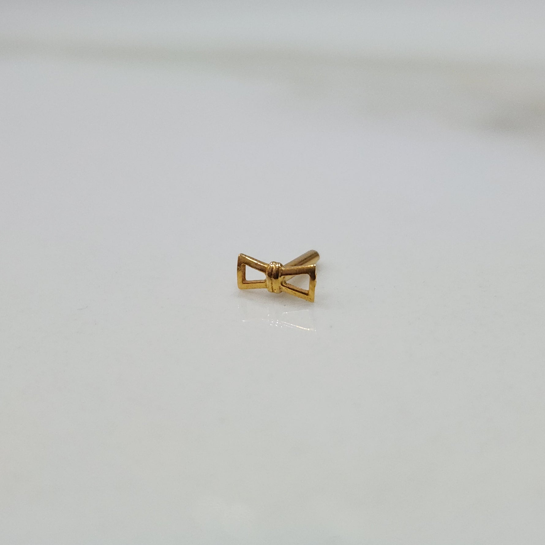 Ribbon Whisper gold nose pin with delicate bow-tie inspired design placed on a flat surface in close-up view