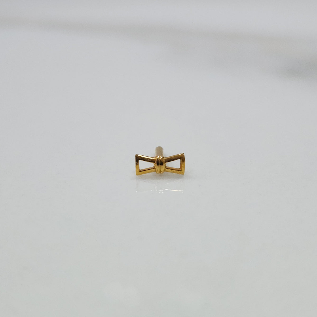 Ribbon Whisper gold nose pin featuring an elegant bow-tie inspired design placed on a flat white surface