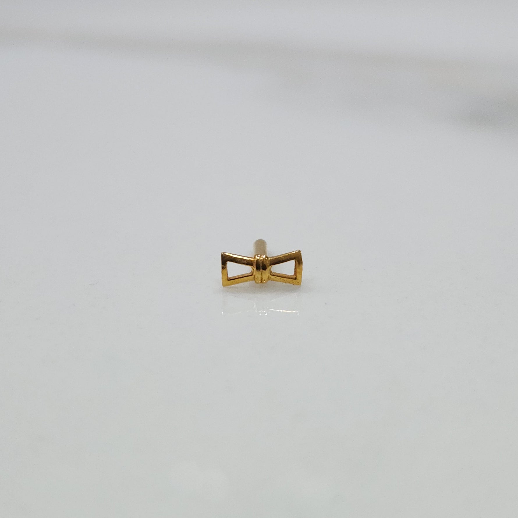 Ribbon Whisper gold nose pin featuring an elegant bow-tie inspired design placed on a flat white surface
