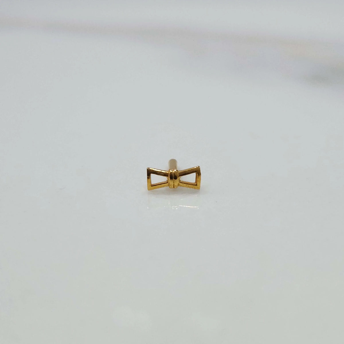 Close up of small hourglass gold nose pin design placed on white background ideal for elegant minimal look